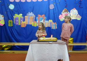 Dwoje dzieci stoi przy cieście urodzinowym.