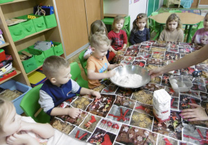Nauczyciel podaje dziecku miskę z mąką.