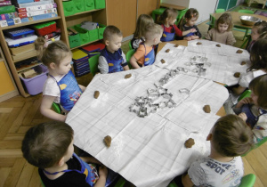 Dzieci siedzą przy stolu. Na stole leżą foremki do pierników.
