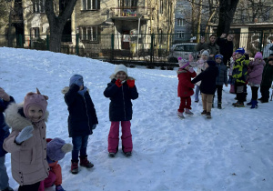 Inna grupa dzieci stoi i macha rękami.