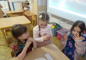 Dziewczynki siedzą przy stole i obserwują eksperymenty.