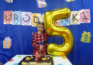 Dziewczynka stoi z balonem w kształcie cyfry 5.