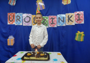 Chłopiec stoi przy cieście urodzinowym.