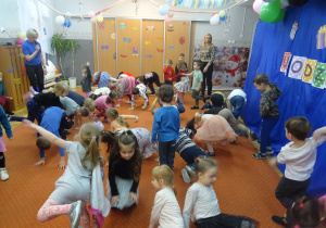 Dzieci klęczą na dywanie z jedną ręką podniesioną do góry.