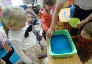 Dziewczynka wkłada drewniany patyczek do plastikowego pojemnika.