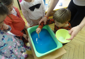 Chłopiec wkłada drewniany patyczek do plastikowego pojemnika.