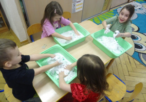 Inna grupa dzieci siedzy przy stoliku z plastikowymi pojemnikami.