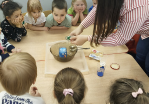 Nauczycielka wlewa wodę do słoika z niebieskim proszkiem.
