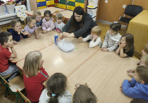 Wszytkie dzieci siedzą przy stole, nauczycielka wykonuje eksperyment.