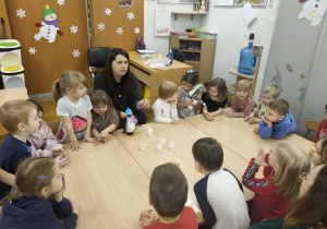 Dzieci i nauczycielka siedzą przy stole i wspólnie rozmawiają o eksperymencie.
