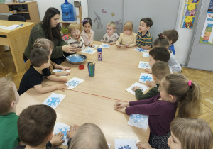 Nauczycielka rozdała dzieciom niebieskie śnieżynki na białej kartce.