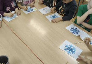 Dzieci podczas kolorowania śnieżynek na papierze.