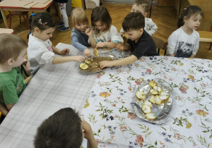 Grupa dzieci siedzi przy stole i zbiera nasionka.