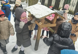 Grupa dzieci stoi przy karmniku.