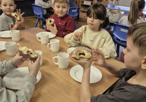 Grupa dzieci siedzi przy stoliku i je pączki.