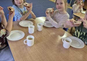 Kolejna grupa dzieci siedzi przy stoliku i je pączki.