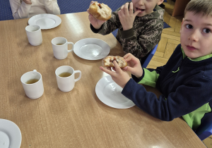 Inna grupa dzieci siedzi przy stoliku i je pączki.