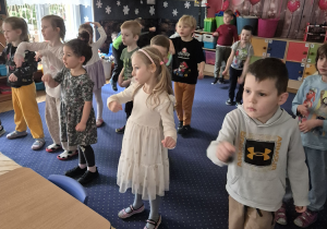 Grupa dzieci tańczy w sali przedszkolnej.