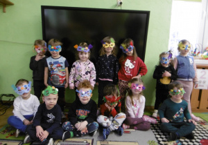 Grupa dzieci stoi obok siebie razem. Na twarzy mają maski karnawałowe.