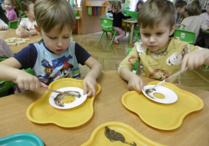 Dwoje innych dzieci maluje talerzyk papierowy.