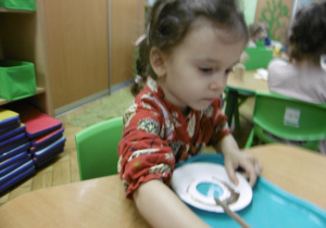 Dziewczynka podczas malowania talerzyka papierowego.