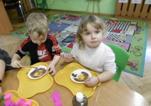 Dwoje innych dzieci siedzi obok siebie. dziewczynka trzyma w ręku pędzel i papierowy talerzyk.