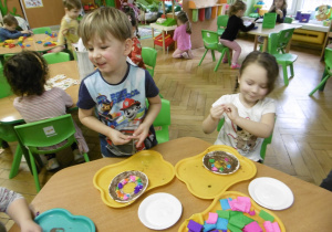 Dwoje dzieci siedzi przy stoliku i wykonuje papierowe talerze.