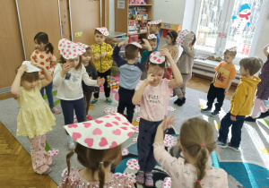 Grupa dzieci tańczy z papierowymi serduszkami na głowie.