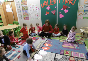 Grupa dzieci siedzi na dywanie z czerowonym serduszkiem.