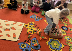 Dziewczynka sięga po pluszową marchewkę.