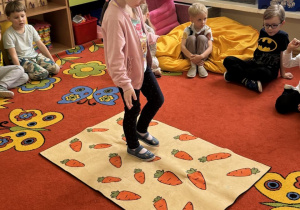 Dziewczynka idzie po marchewkowym dywanie.