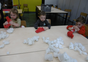 Troje dzieci siedzi przy stole z czerwonymi skarpetami.