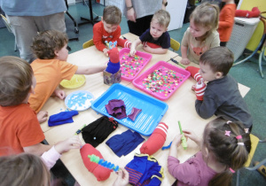 Grupa dzieci stoi przy stoliku pełnym kolorowych elementów.