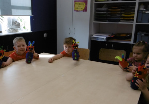 Grupa dzieci siedzi przy stoliku z wykonanymi przez siebie pracami.