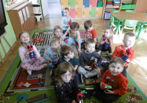 Grupa dzieci siedzi na dywanie w sali przedszkolnej z wykoanaymi przez siebie" Skarpeciakmi"