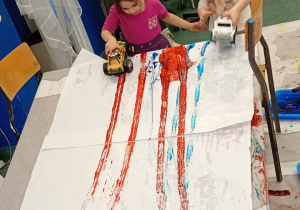 Dzieci malują za pomocą opon od zabawkowych aut.