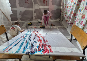 Dzieci malują farbami za pomocą zabawkowych aut.