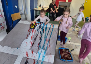 Dzieci malują farbami za pomocą zabawkowych aut.