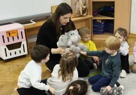 Nauczyciel siedzi na dywanie i w rękach trzyma maskotkę.