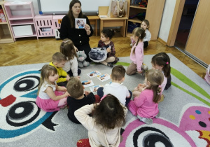 Nauczyciel w otoczeniu dzieci trzyma ilustrację z podobizną kota.