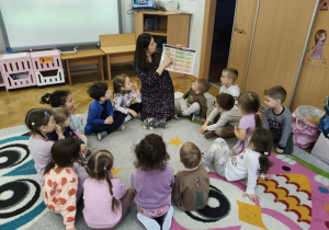 Nauczyciel siedzi na dywanie, w ręku trzyma planszę.