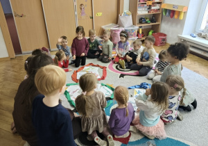 Grupa dzieci siedzi na dywanie. Na środku znajdują się kolorowe koła.