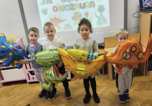 Czworo dzieci stoi z dmuchanymi dinozaurami.