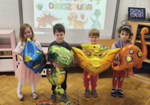 Czworo innych dzieci stoi z dmuchanymi dinozaurami.