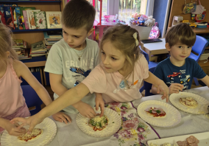 Dziewczynka sięga po dodatki na swój kawałek ciasta.