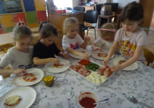 Dzieci podczas układania swoich kawałków ciasta na pizzę.