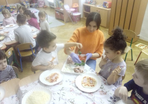 Nauczycielka podaje dzieciom dodatki do pizzy.