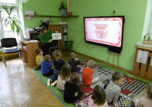 Grupa dzieci siedzi przed monitorem.