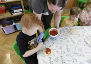 Pani z obsługi pomaga chłopcu nałożyć sos pomidorowy.