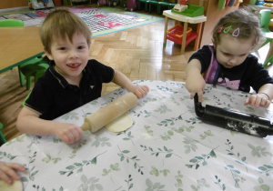 Dwoje innych dzieci wałkuje swoje kawałki ciasta.